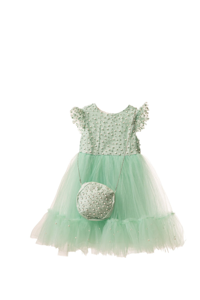 Girl wearing a green party dress with white polka dots, ruffled sleeves, and a tulle skirt, holding a matching green handbag